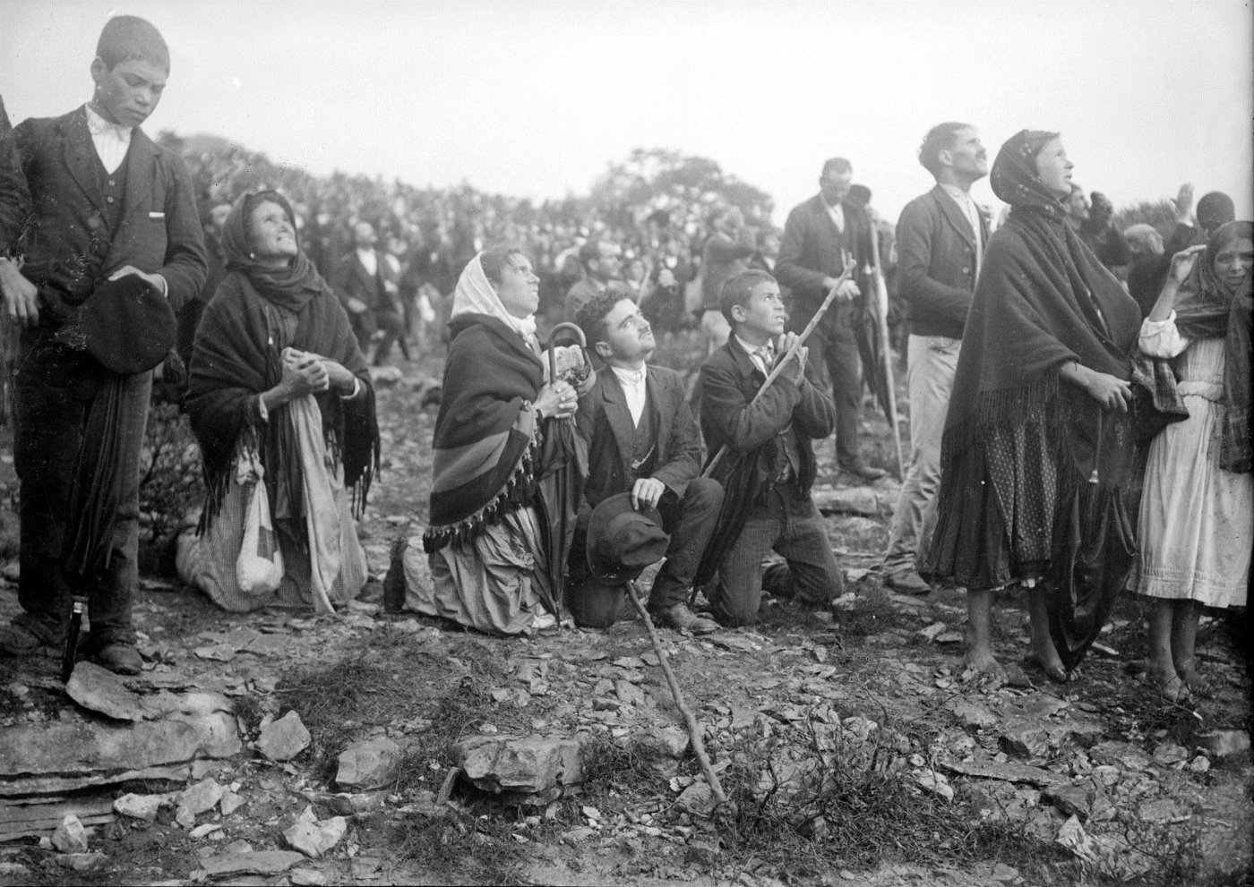 A large crowd in a field looks upward on 13 October 1917 at Fátima